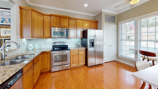 kitchen featuring sink, light stone counters, light hardwood / wood-style flooring, ornamental molding, and appliances with stainless steel finishes