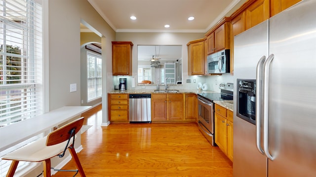 kitchen featuring sink, ornamental molding, stainless steel appliances, light stone countertops, and light hardwood / wood-style flooring