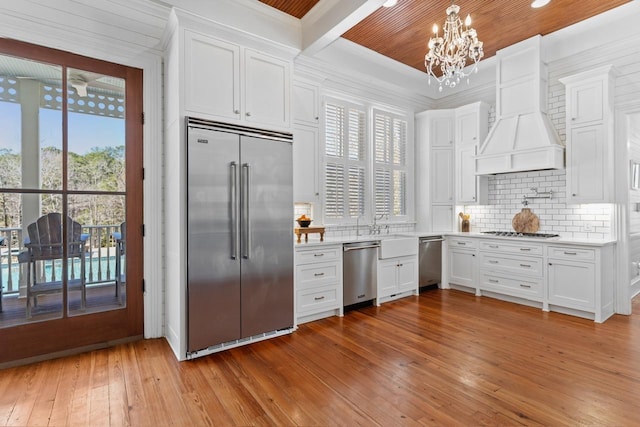 1011 Dogwood Dr, Greensboro, GA 30642 - kitchen featuring light wood-style floors, an inviting chandelier, tasteful backsplash, appliances with stainless steel finishes, and custom range hood