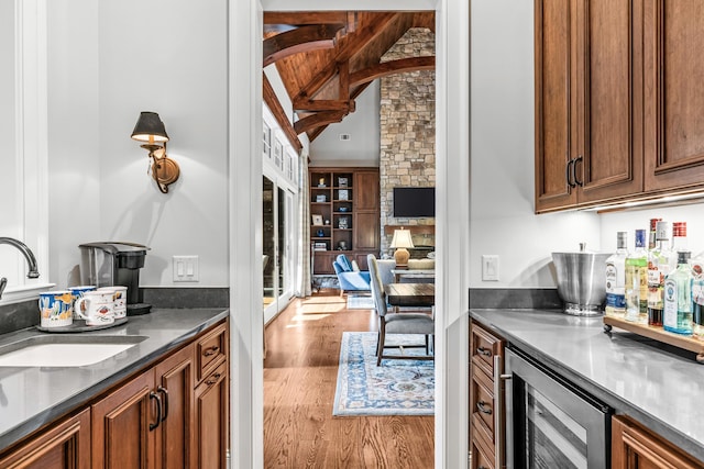 kitchen featuring sink, lofted ceiling with beams, light wood-type flooring, beverage cooler, and a fireplace