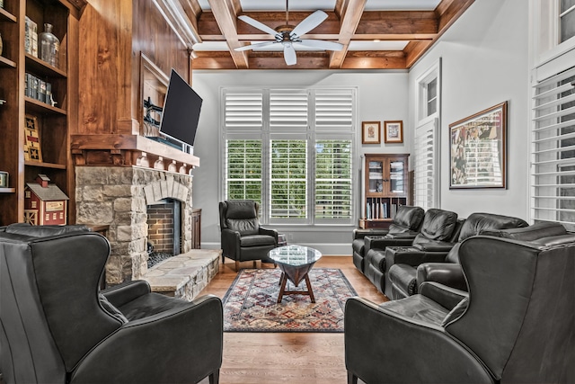 living room featuring coffered ceiling, a stone fireplace, beamed ceiling, hardwood / wood-style flooring, and ceiling fan