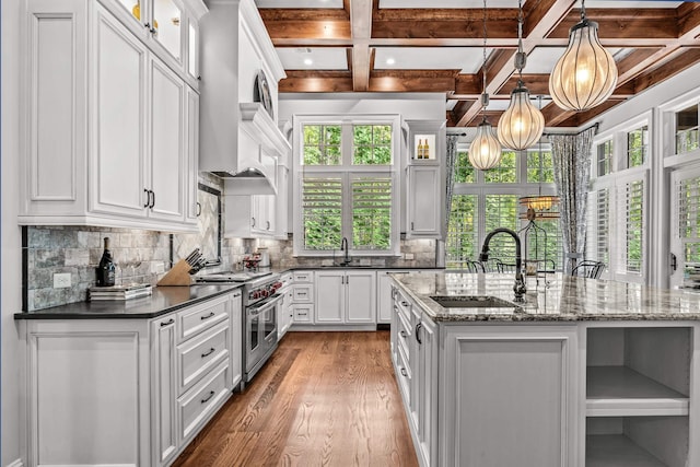 kitchen with pendant lighting, sink, double oven range, white cabinets, and a center island with sink