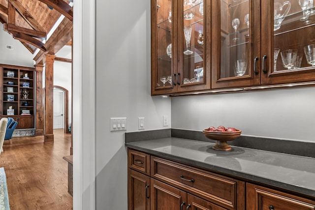 bar featuring dark stone countertops, dark brown cabinets, and hardwood / wood-style floors