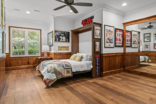 bedroom with ceiling fan, ornamental molding, wooden walls, and wood-type flooring