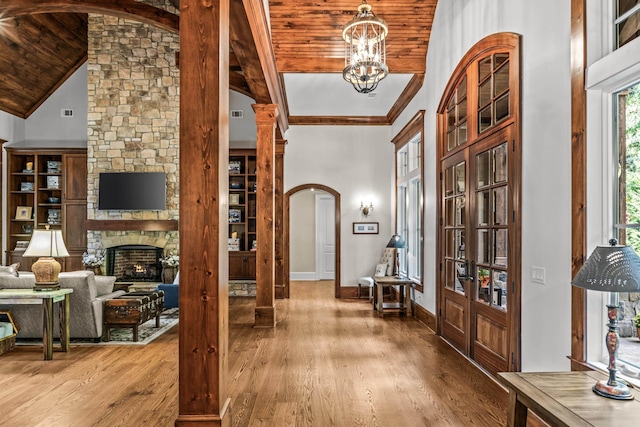 entrance foyer with wood-type flooring, a stone fireplace, high vaulted ceiling, and a notable chandelier