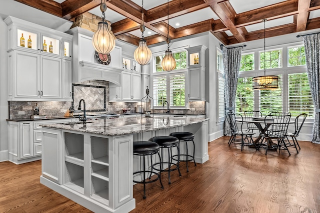 kitchen with white cabinetry, dark stone countertops, an island with sink, and pendant lighting