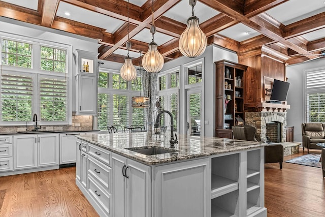 kitchen with an island with sink, sink, dark stone countertops, and light wood-type flooring