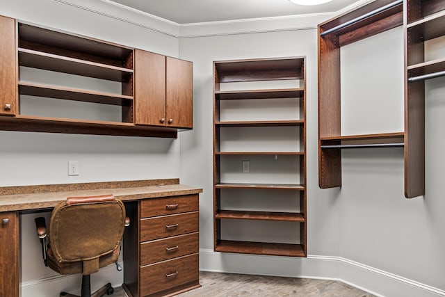 unfurnished office featuring ornamental molding, built in desk, and light hardwood / wood-style flooring