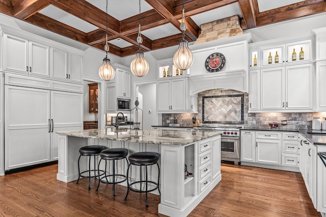 kitchen with white cabinetry, built in appliances, hanging light fixtures, dark stone countertops, and an island with sink