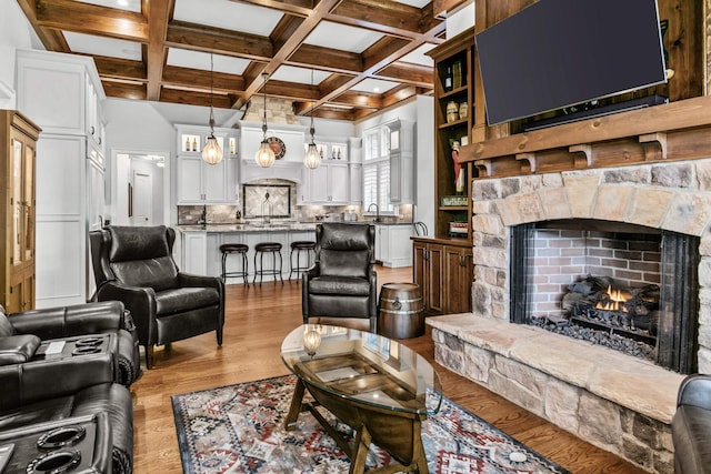 living room featuring coffered ceiling, a stone fireplace, light hardwood / wood-style floors, and beamed ceiling