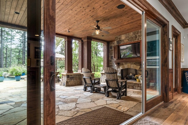 unfurnished sunroom featuring ceiling fan, wooden ceiling, and an outdoor stone fireplace