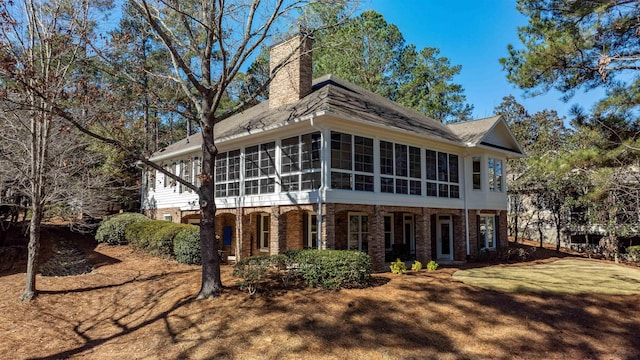 rear view of house featuring a sunroom, a chimney, a lawn, and brick siding