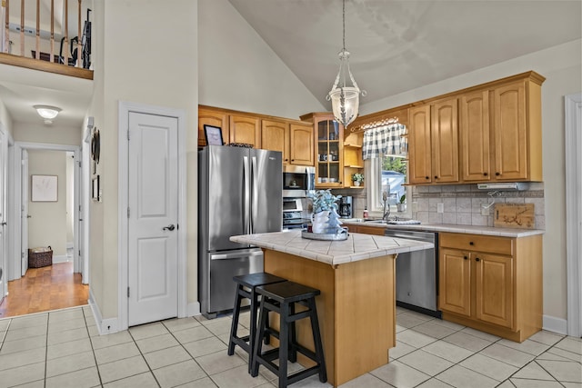 kitchen with light tile patterned floors, appliances with stainless steel finishes, backsplash, tile counters, and a kitchen island