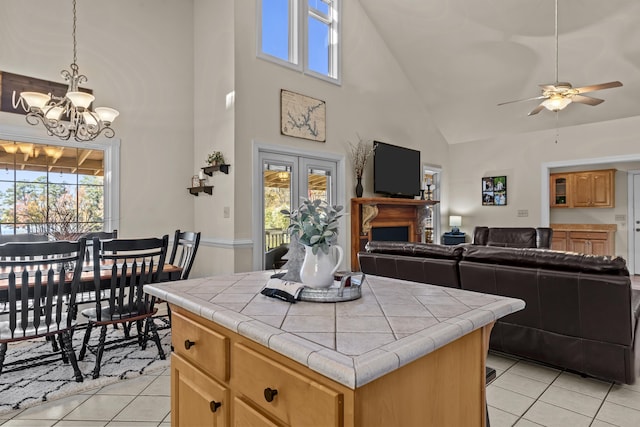 kitchen with light tile patterned flooring, ceiling fan with notable chandelier, tile countertops, decorative light fixtures, and a center island