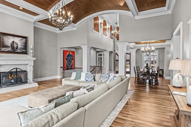 living room featuring crown molding, wood-type flooring, decorative columns, and a notable chandelier