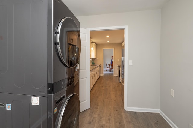 clothes washing area with stacked washer / drying machine, hardwood / wood-style floors, and sink