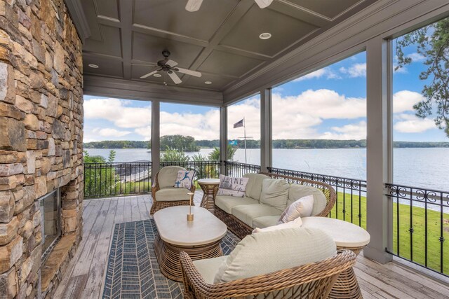 sunroom featuring a water view, ceiling fan, coffered ceiling, and an outdoor stone fireplace