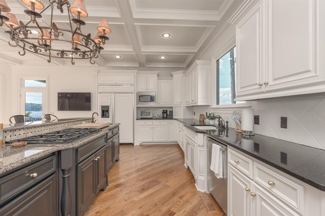 kitchen with built in appliances, sink, dark stone counters, and white cabinets