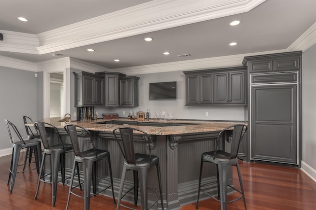 kitchen with a breakfast bar, dark hardwood / wood-style floors, ornamental molding, a kitchen island, and dark stone counters