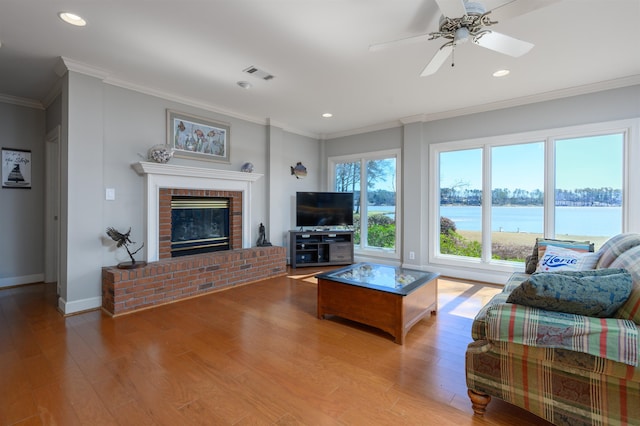 living area with visible vents, a fireplace, light wood finished floors, crown molding, and baseboards