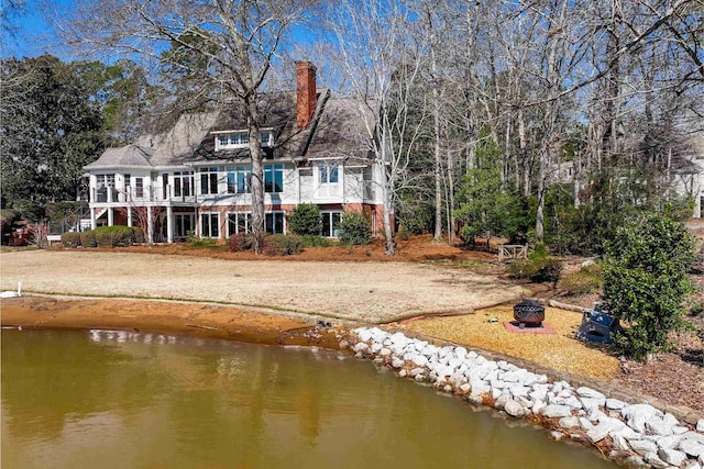 rear view of property featuring a water view, a fire pit, and a chimney