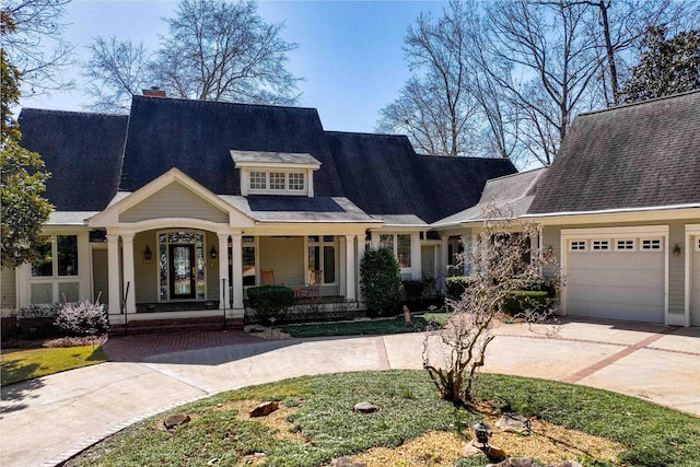 view of front facade with concrete driveway, a porch, an attached garage, and a chimney