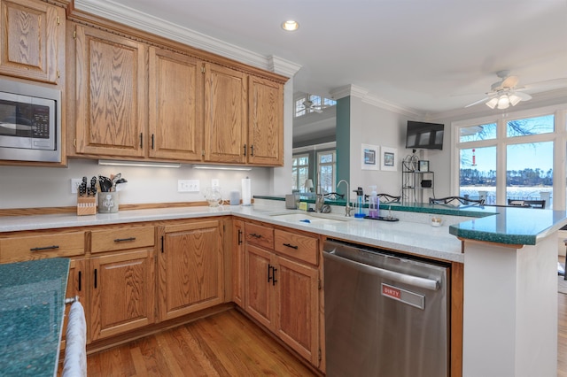 kitchen with ornamental molding, a sink, appliances with stainless steel finishes, a peninsula, and light wood finished floors