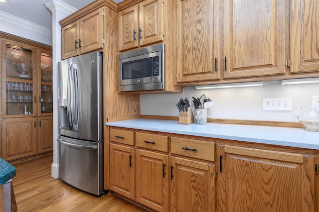 kitchen with light wood finished floors, light countertops, appliances with stainless steel finishes, crown molding, and brown cabinets