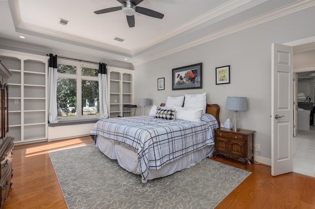 bedroom with visible vents, a raised ceiling, wood finished floors, and crown molding