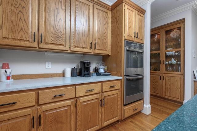 kitchen with light wood-style flooring, double oven, brown cabinetry, crown molding, and light countertops