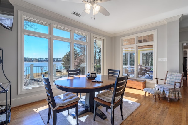 dining area featuring wood finished floors, visible vents, a water view, and a healthy amount of sunlight