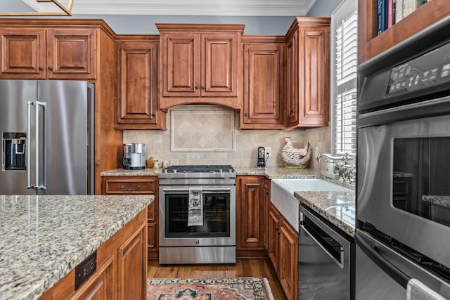 kitchen featuring light stone counters, crown molding, stainless steel appliances, a sink, and wood finished floors