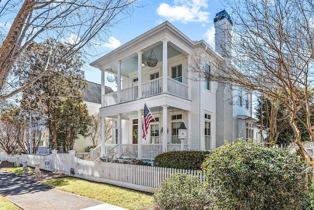 greek revival house with a fenced front yard, a chimney, a porch, ceiling fan, and a balcony