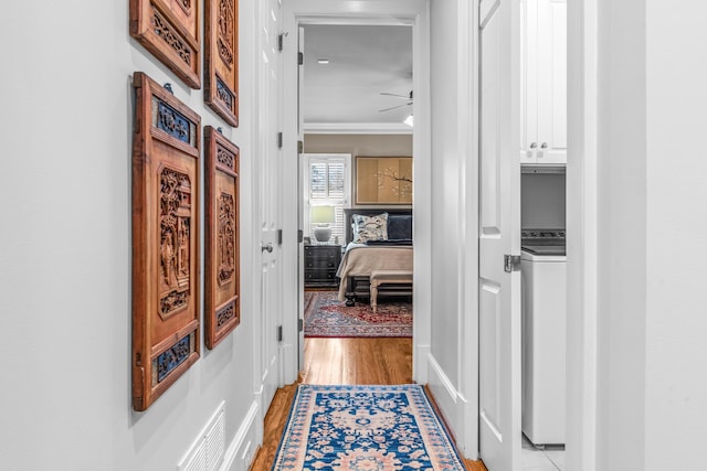 corridor featuring crown molding, washer / clothes dryer, visible vents, and light wood-style floors