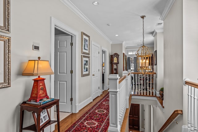 hallway featuring crown molding, recessed lighting, light wood-style flooring, an inviting chandelier, and an upstairs landing