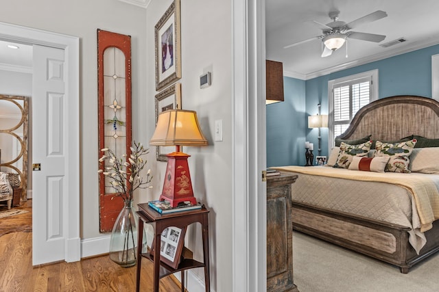 bedroom with wood finished floors, a ceiling fan, baseboards, visible vents, and crown molding