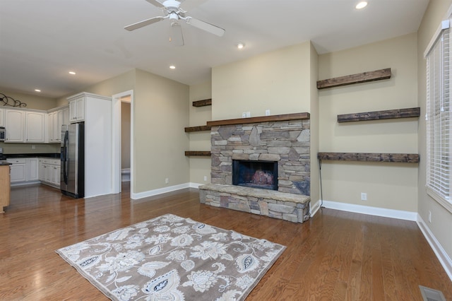 living room with dark wood-type flooring, ceiling fan, and a stone fireplace