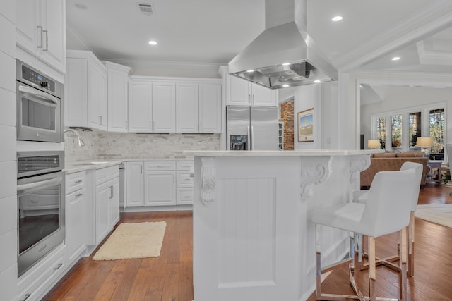 kitchen featuring sink, appliances with stainless steel finishes, white cabinetry, ornamental molding, and island exhaust hood