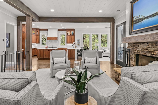 living room featuring ornamental molding, beam ceiling, sink, and light hardwood / wood-style flooring