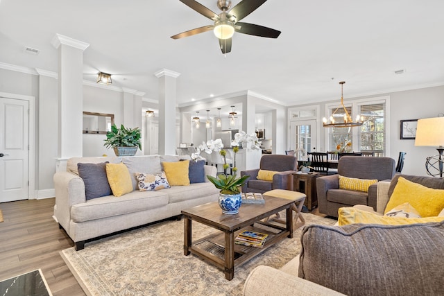 living room with decorative columns, crown molding, ceiling fan with notable chandelier, and light wood-type flooring