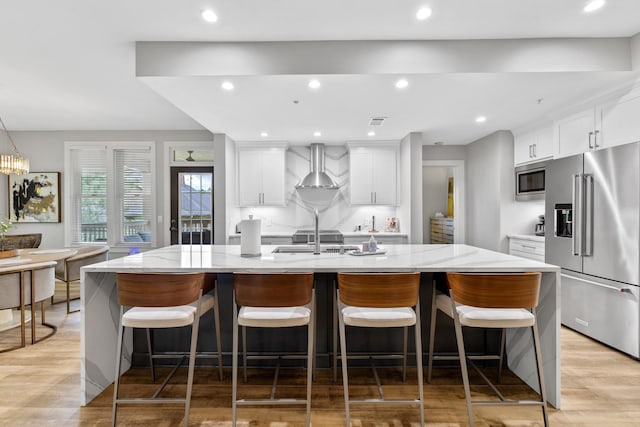 1010F Tailwater, Greensboro, GA 30642 - kitchen featuring wall chimney range hood, appliances with stainless steel finishes, a kitchen island with sink, and light wood-type flooring
