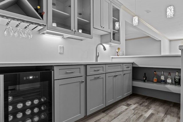 kitchen with gray cabinetry, beverage cooler, hanging light fixtures, crown molding, and dark wood-type flooring