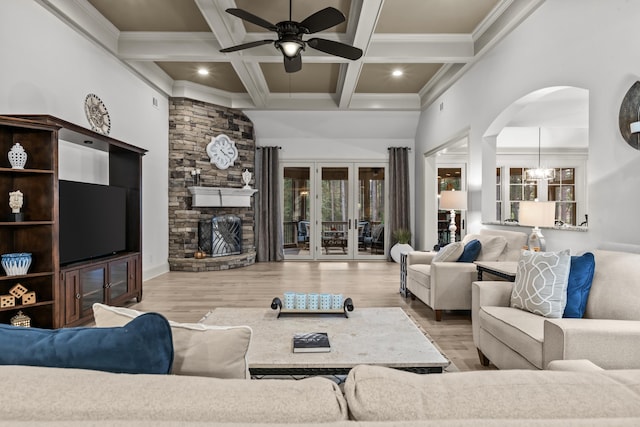 living room with coffered ceiling, beam ceiling, a stone fireplace, and light hardwood / wood-style floors