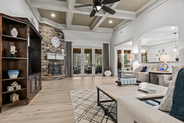 living room featuring coffered ceiling, a stone fireplace, beam ceiling, and light hardwood / wood-style flooring