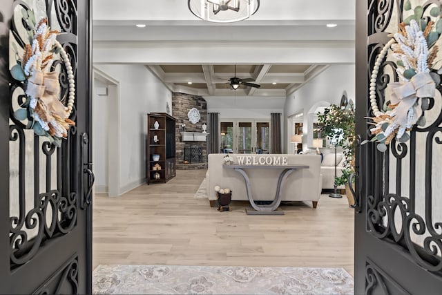 entrance foyer with coffered ceiling, a stone fireplace, light hardwood / wood-style flooring, beamed ceiling, and ceiling fan