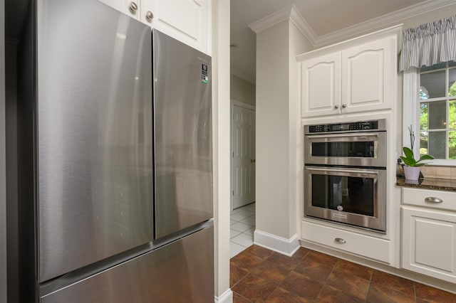 kitchen featuring ornamental molding, appliances with stainless steel finishes, dark stone countertops, and white cabinets