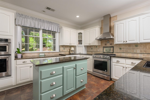 kitchen featuring wall chimney exhaust hood, dark stone countertops, a kitchen island, stainless steel appliances, and white cabinets