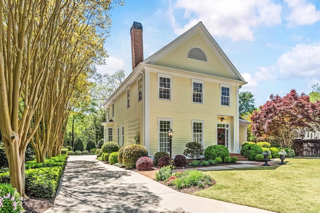 view of side of property with a yard, fence, driveway, and a chimney