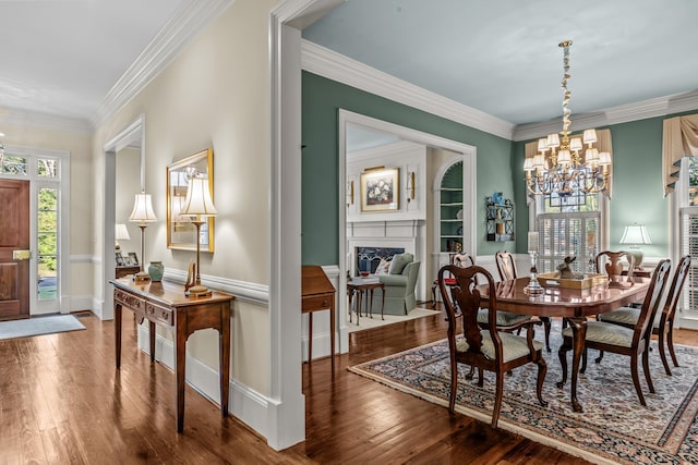dining room with a high end fireplace, hardwood / wood-style floors, an inviting chandelier, and crown molding