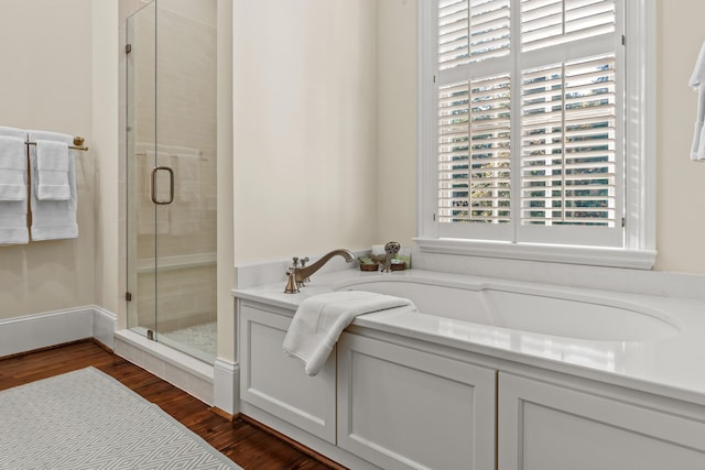 full bath featuring a bath, a shower stall, and wood finished floors